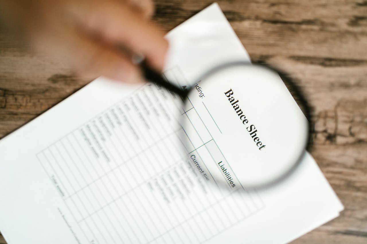 Close-up of a balance sheet under a magnifying glass on a wooden table.